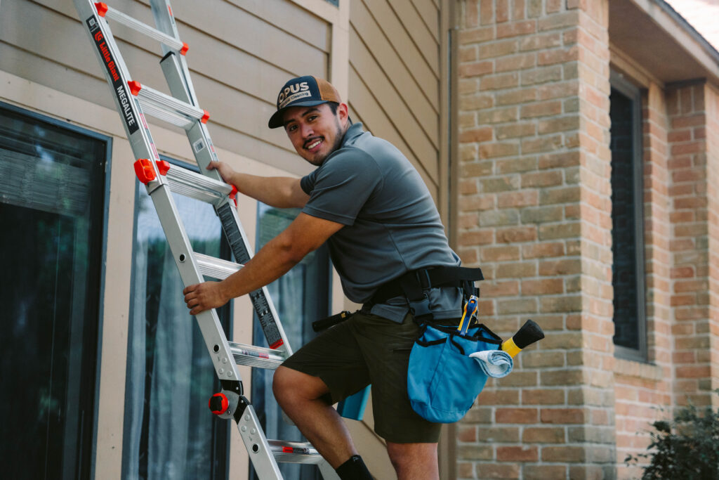 Window cleaning technician on an extension ladder with professional cleaning tools in Houston, TX.